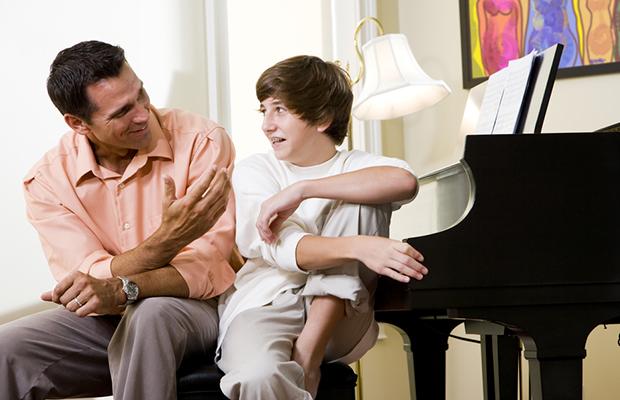 man and teen boy sitting at piano talking